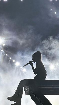 a person sitting on a bench with a microphone in their hand and fireworks behind them