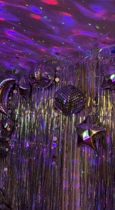 many shiny objects hanging from the ceiling in front of purple and green lights with stars on them