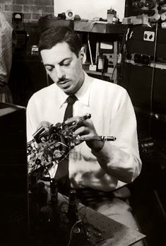 black and white photograph of a man working on an electronic device in a room with other people