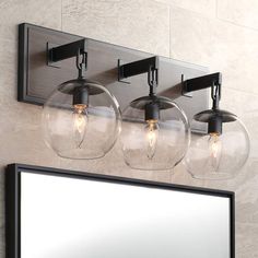 three clear globe lights are hanging from the wall above a mirror and light fixture in a bathroom