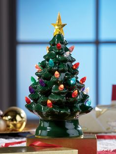 a ceramic christmas tree with lights on it sitting on a table in front of a window