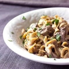 a white bowl filled with pasta and meat on top of a purple cloth covered table