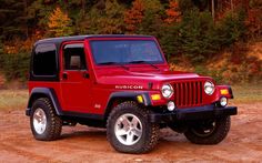 a red jeep is parked in the dirt