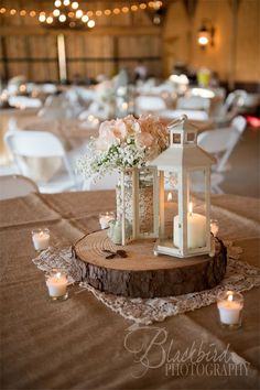 a table topped with a white lantern and flowers on top of a piece of wood