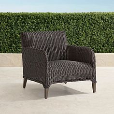 a brown chair sitting on top of a cement floor next to a green hedge covered wall