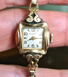 "This is a gorgeous Benrus 10K yellow rolled gold plated ladies watch that is currently NON working. I am not a watch expert, nor have I had it tested or serviced, it is being sold AS IS.  The face is a square with a pearly ivory face and gold hands and numerals. There is a lovely scroll design around the watch face that really sets it apart. The watch is marked 10k RGP on the back. This watch is approximately 6\". The band is a vintage segmented stretch band that also has a lot of visual intere Antique Engraved Jewelry And Watches For Wedding, Victorian Yellow Gold Watches For Anniversary, Victorian Yellow Gold Anniversary Watch, Antique Hallmarked Watches For Wedding, Antique Round Watches For Wedding, Heirloom Quartz Watches For Wedding, Collectible Gold Art Deco Jewelry And Watches, Victorian Gold Watch For Weddings, Gold Victorian Watches For Weddings