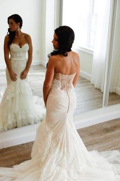 a woman standing in front of a mirror wearing a wedding dress and looking at herself in the mirror