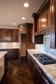 an empty kitchen with wooden cabinets and marble counter tops, along with dark wood flooring