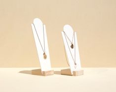 two pieces of wood with necklaces on them sitting next to each other in front of a beige wall