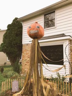 an orange pumpkin sitting on top of a wooden pole in front of a house with halloween decorations around it