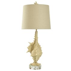 a table lamp with a white shade on it and a shell shaped base in the center