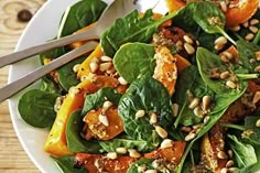 a white plate topped with spinach salad and oranges on top of a wooden table