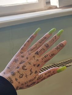 a person's hand with writing on it and green nail polish, in front of a window