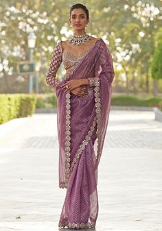 Introducing our deep lilac saree, crafted from luxurious organza and embellished with an intricate gold border enhanced with mirror work and rose gold embroidery. Paired with a sweetheart neckline full-sleeves blouse featuring real hand-cut mirror embroidery and a statement cuff, this set is a true masterpiece. The tasselled back on the blouse is sure to capture attention at any occasion. Perfect for Sangeet or reception. Composition : Saree - Organza, Blouse - Georgette Care: Dry Clean Only and Vacuum Storage This product can be customized for sleeves, length and colour Delivery : 6-8 weeks as the product is hand crafted. Check Size Guide or choose MySize for free customisation (All Sizes above XL can be made at 15% additional cost) For more information and sizes please contact fabiliciou Organza Sarees With Full Sleeve Blouse, Saree Long Blouse Designs Latest, Full Sleeves Blouses Saree, Designer Sarees For Reception, Full Sleeves Saare Blouse, Sequin Saree Blouse Designs Full Sleeves, Full Hand Saree Blouse, Saree Blouses Full Sleeves, Full Sleeve Blouse Designs Saree Indian Weddings