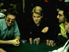 three men sitting at a table with poker chips in front of them and one man holding his hand up