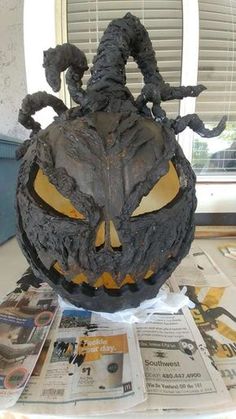 a halloween pumpkin with an evil face on top of it and some newspaper next to it