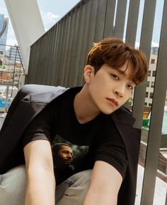 a young man sitting on top of a cement bench next to a metal fence and building