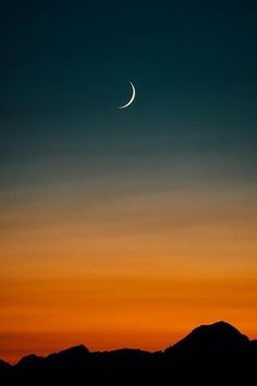 the moon is seen in the sky over mountains at sunset, with an orange and blue hue