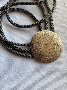 Floral stamped brass Medallion bolo tie necklace on light gold/black patterned nylon cord. Vintage Formal Jewelry With Adjustable Length, Vintage Jewelry With Adjustable Length For Formal Occasions, Vintage Lariat Jewelry With Sliding Knot, Antique Finish Adjustable Round Jewelry, Festival Gold Jewelry With Adjustable Cord, Gold Jewelry With Sliding Knot For Festival, Vintage Necklace With Adjustable Cord For Festivals, Vintage Black Lariat Jewelry, Adjustable Etched Gold Jewelry