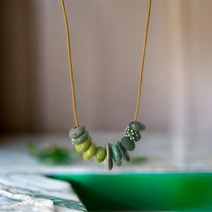 a necklace with green beads hanging from it's side on a table next to a bowl