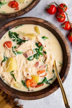 two bowls of soup with tomatoes and spinach on the side next to a spoon