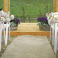 an outdoor ceremony setup with chairs and flowers on the aisle, overlooking a vineyard area