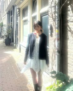 a woman standing in front of a brick building wearing black boots and a white dress