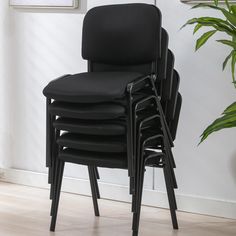 four black stacking chairs in front of a potted plant on a hard wood floor