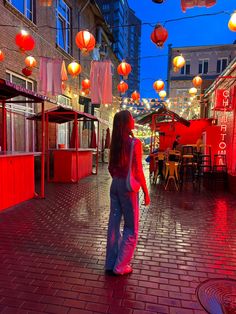 a woman is walking down the street in front of some red lanterns hanging from the ceiling