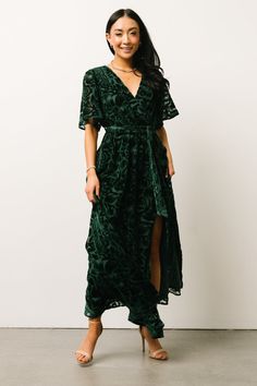 a woman standing in front of a white wall wearing a green velvet dress with an asymmetrical design