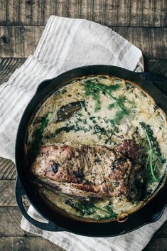 a skillet filled with meat and vegetables on top of a white napkin next to a wooden table