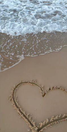 a heart drawn in the sand at the beach with waves coming in and crashing on it