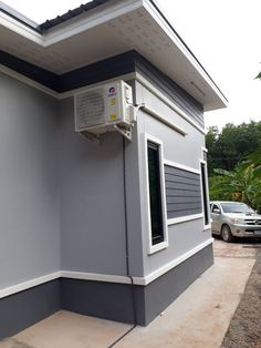 an air conditioner mounted on the side of a gray and white building next to a car