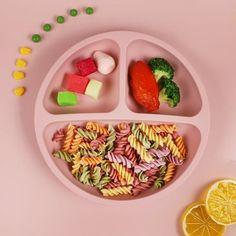 a plate filled with pasta and veggies on top of a pink surface next to lemon slices