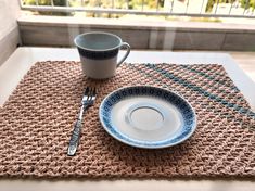 a place mat with a coffee cup on it next to a fork and spoon sitting on top of a table