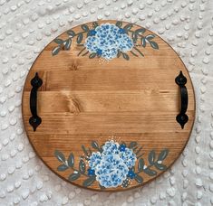 a wooden board with blue flowers painted on the side and black handles sitting on a white tablecloth