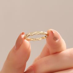 a woman's hand holding a gold ring with braiding on the inside of it