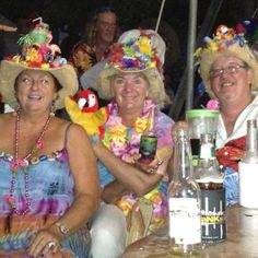 three women sitting at a table with hats on their heads and drinks in front of them