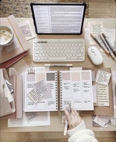 a person's hand is writing on a notebook next to a laptop and keyboard