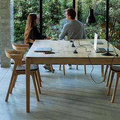 two people sitting at a table with laptops on it in front of large windows