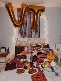 a bed topped with lots of food and balloons in the shape of letter v on top of it