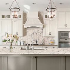 a kitchen with white cabinets and marble counter tops, two pendant lights over the island