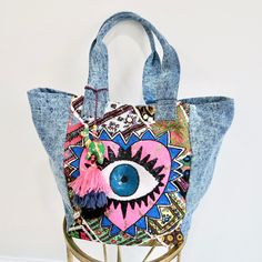 Denim never goes out of style, and our Denim Tote is designed to be your go-to bag for years to come. With stunning hand beading and embroidery, this tote is a true showstopper, perfect for any occasion. Key Benefits & Features: Hand Beaded & Embroidered: Eye-catching details make this tote a standout accessory. Spacious Design: Roomy enough for shopping, travel, or an overnight stay. Dimensions: 13" x 17.5" x 12.5", with shoulder straps, a magnetic button closure, and interior zip pockets for e Blue Embroidered Denim Bags, Embroidered Denim Bags For Everyday Use, Trendy Tote Bag For Festivals, Bohemian Blue Canvas Bag, Quick Getaway, Denim Tote, Easy Organization, Shopping Travel, Ethical Fashion