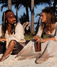 two people are sitting on the sand and one is holding a bottle