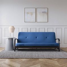 a blue couch sitting on top of a wooden floor next to a white vase and lamp