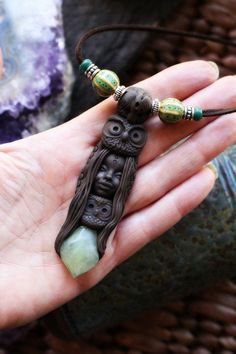 a person is holding an owl necklace with beads on it's fingers and wearing a bracelet