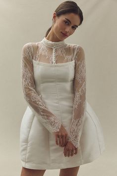 a woman in a short white dress with sheer sleeves and lace on the neckline