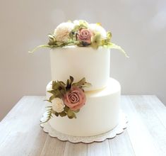 a three tiered white cake with flowers on the top and bottom, sitting on a wooden table