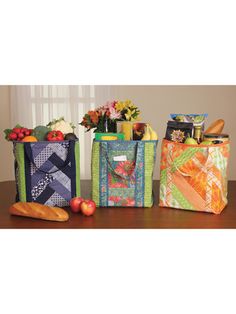 three colorful bags sitting on top of a wooden table next to each other with fruit and vegetables in them