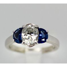 This is part of Chairish’s Fine Jewelry assortment.  Diamond Ring with Half Moon Sapphire Sides  This ring is unusual as it has a center oval cut Diamond of 1.20 carats and enhanced by moon cut Sapphires of 1/2 carat each totaling 2.20 tcw. The ring is sized 6 1/4 and can be enlarged or made smaller. It weighs 4.8 grams. This ring is perfect for a wedding, anniversary, or birthday. The Diamond is a H-I in color and VS2- SI in clarity. The Sapphires are beautiful eye clean and intense Sapphire Bl Oval Sapphire Ring In Diamond White, Oval Sapphire Diamond Ring In Diamond White, Oval Sapphire Diamond White Ring, White Oval Sapphire Ring, Oval Sapphire Three-stone Diamond Ring, Oval Sapphire Three Stone Diamond Ring, Oval Sapphire Ring With Brilliant Cut In Platinum, White Oval Sapphire Gemstone Ring, Platinum Three-stone Oval Rings